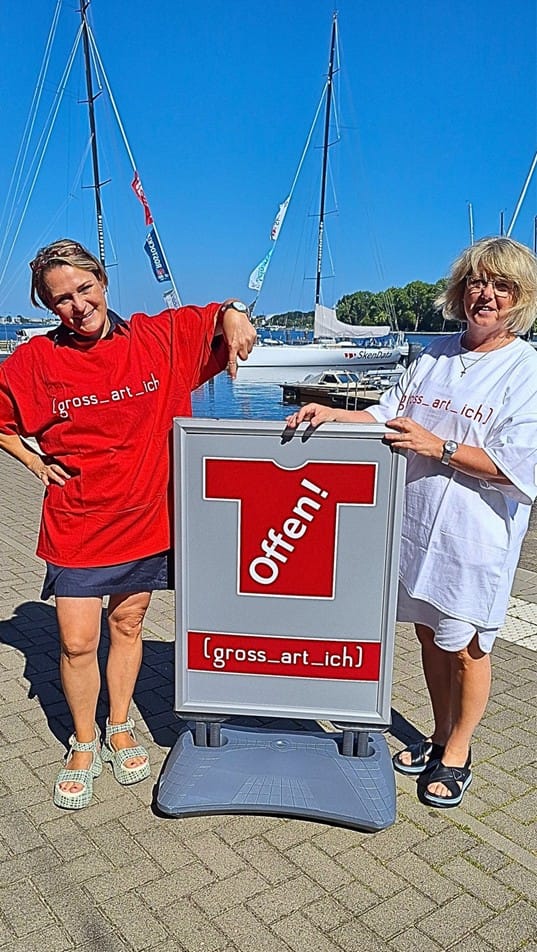 Anke Bahr und ihre Mitarbeiterin präsentieren das Logo des Modehauses "gross-art-ich" für Grosse Grössen und Lange Längen Im Rostocker Stadthafen.